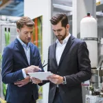 Two businessmen in factory looking at tablet